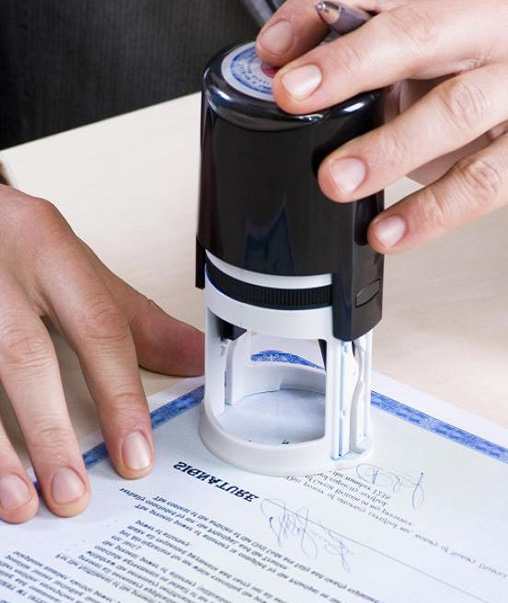 Hand pressing a self-inking stamp onto a signed document, representing the notarial verification step